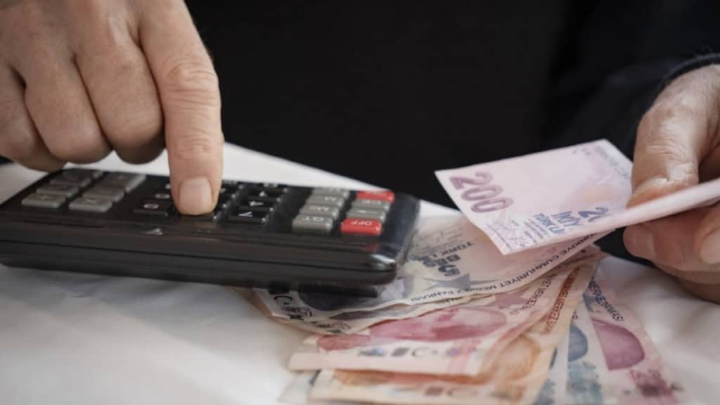 200 TL'lik banknotları elinde tutan bir kişi hesap makinesinde hesaplama yapıyor